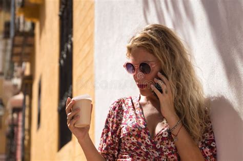 Middle Aged Blonde Woman Wearing A Flowered Dress And Sunglasses With A Glass Of Coffee In Her