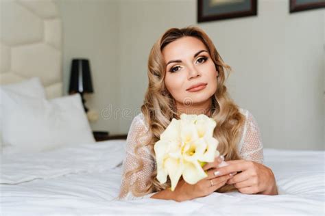 Beautiful Blonde In A White Peignoir With A Bouquet Of Flowers Lying In Bed Stock Photo Image