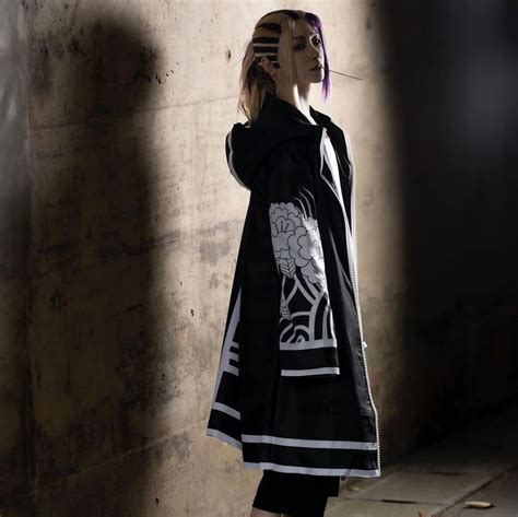 A Woman Standing Next To A Wall Wearing A Black Coat