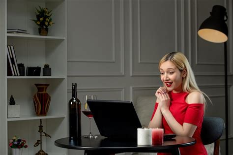 Amour virtuel jolie fille blonde en robe rouge à distance date avec vin souriant Photo Gratuite