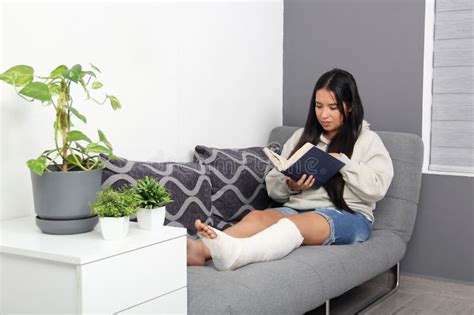 30 Year Old Latina Woman Reads A Book In Her Living Room While Recovering From Her Leg That Was