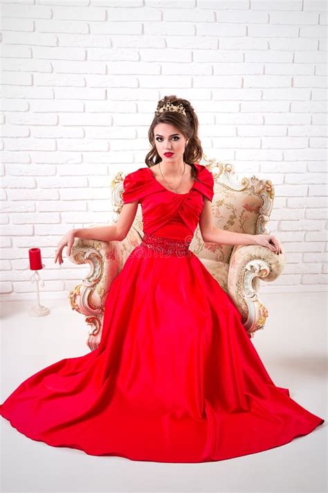 Elegant Woman In A Long Red Dress Sitting On A Chair Stock Photo