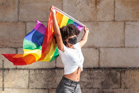 Woman With Face Mask And Afro Hair Holds Up The Lgbtq Flag Of Gay Pride That Moves With The Wind