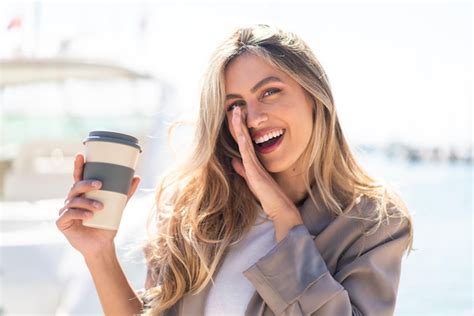 Jolie blonde femme uruguayenne tenant un café à emporter à l extérieur en chuchotant quelque