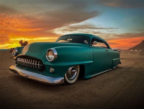 An Old Green Car Parked On The Side Of A Dirt Road At Sunset With