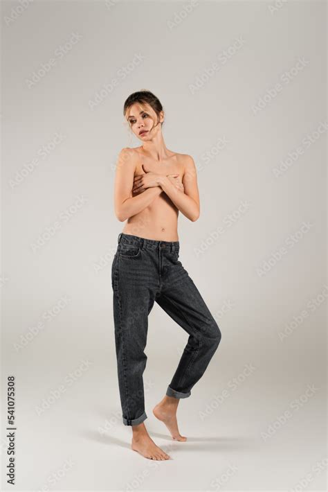 Full Length Of Half Naked Barefoot Woman In Jeans Covering Breast With
