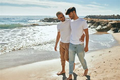 Jovem Casal Gay Sorrindo Feliz Caminhando Na Praia Imagem De Stock Imagem De Pares Retrato