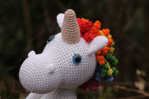 A Crocheted Stuffed Unicorn With Multicolored Mane And Blue Eyes