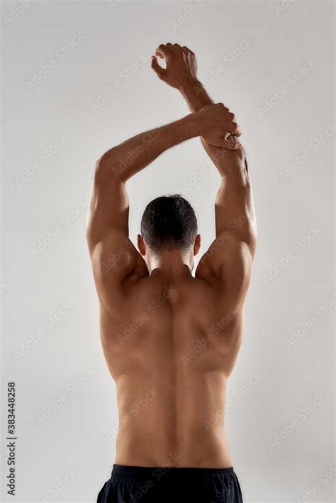 Rear View Of Muscular Man With Naked Torso Raising His Arms Above Head Isolated Over Grey