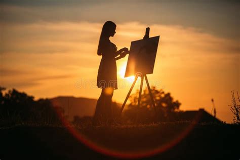 La Silueta De Una Muchacha Del Blonde Pinta Una Pintura En La Lona Con La Ayuda De Las Pinturas