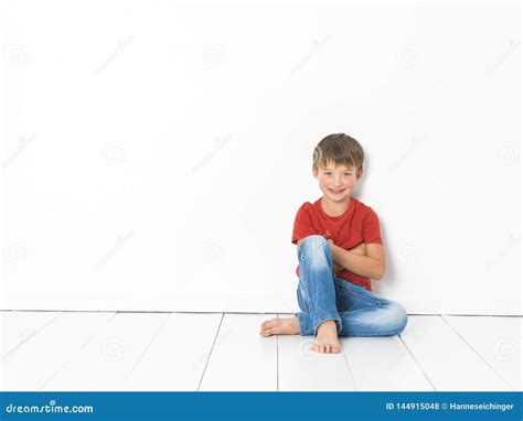 De Leuke En Blonde Jongen Met Rode Overhemd En Jeans Stelt Op Witte Houten Vloer Stock Foto