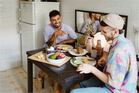 Happy Gay Couple Having Fruits While Sitting At Dining Table In Kitchen Royalty Free Stock