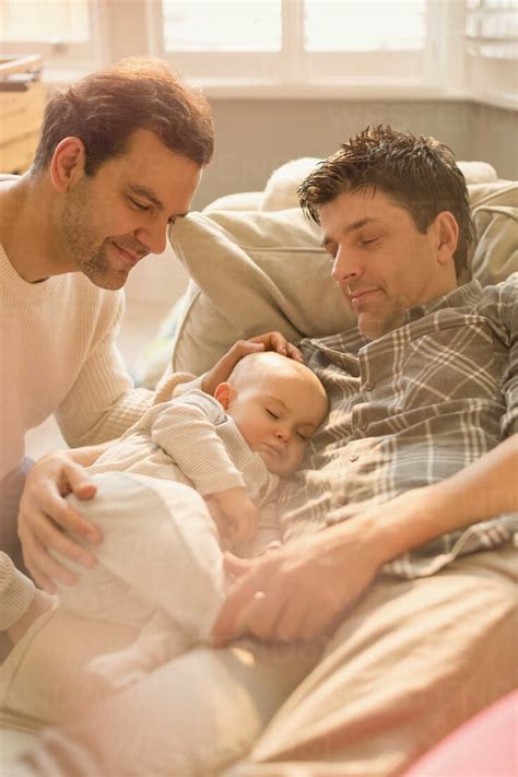 Male Gay Parents Watching Baby Son Sleeping On Sofa Stock Photo