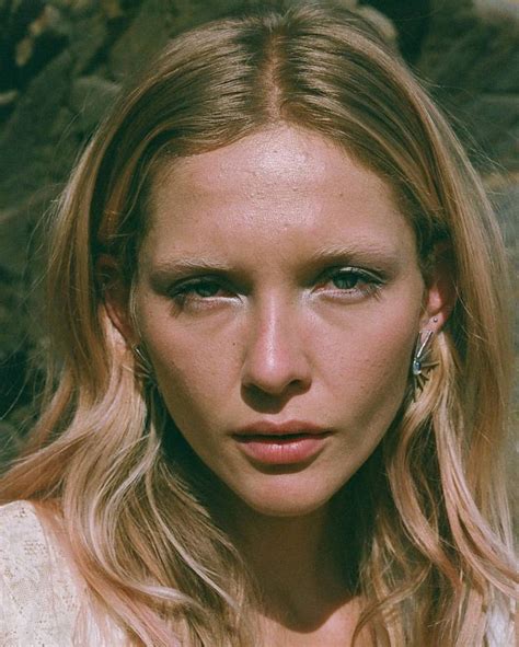 A Close Up Of A Person With Long Blonde Hair And Blue Eyes Wearing Earrings