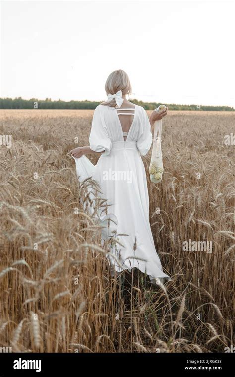 Eine blonde Frau in einem langen weißen Kleid geht in einem Weizenfeld Das Konzept einer