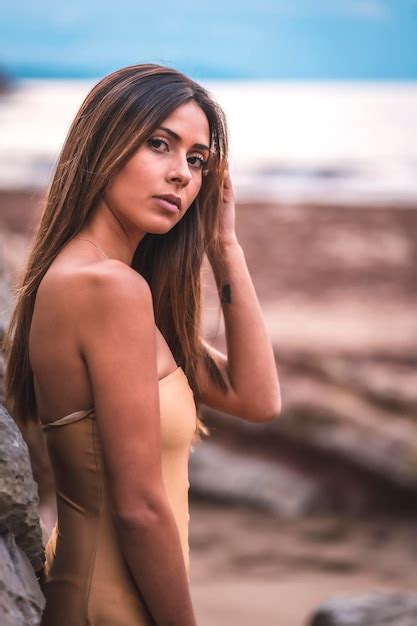 Premium Photo Portrait Of A Brunette Woman In A Swimsuit On A Beach In Summer Leaning On The Rocks