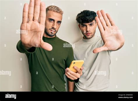 Homosexual Gay Couple Standing Together Using Smartphone With Open Hand Doing Stop Sign With