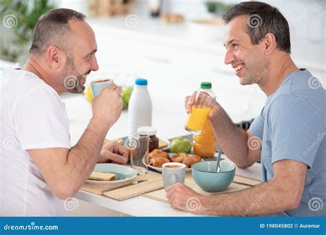Pareja Gay Sonriente Hablando Y Desayunando Juntos Foto De Archivo
