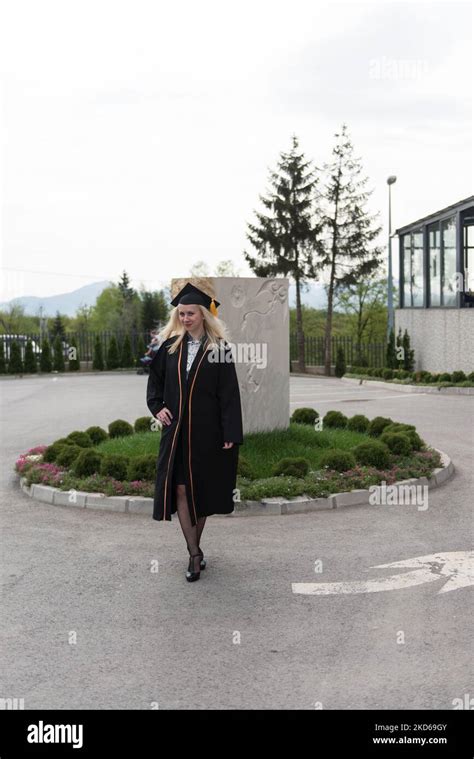 Female Blonde College Or High School Graduate Confidently Wearing Black Cap And Gown At