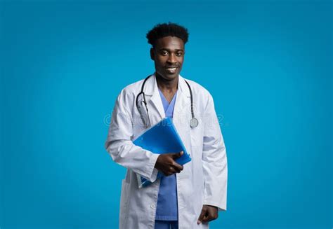 Handsome Black Doctor Posing On Blue Background Holding Folder Stock