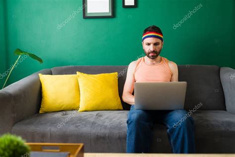 Atractivo hombre gay sentado solo en el sofá y escribiendo en el portátil Latin queer man