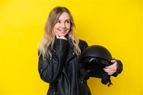 Blonde jeune fille anglaise avec un casque de moto isolé sur fond jaune pensant à une idée tout