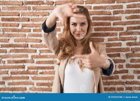 Beautiful Blonde Woman Standing Over Bricks Wall Smiling Making Frame With Hands And Fingers