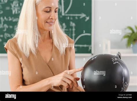 Mature Geography Teacher With Globe In Classroom Stock Photo Alamy