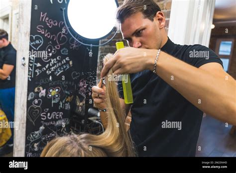 Male Hairdresser Cutting Long Blonde Hair Of A Woman With Scissors