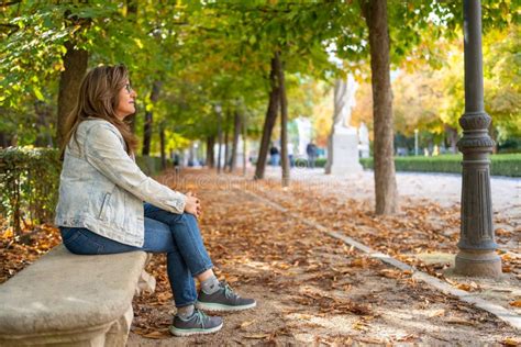 Mature Woman Sitting On A Park Bench In A Relaxed Way And Enjoying The Beautiful Autumn Day