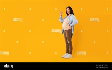 Happy Pregnant Woman Pointing Aside At Free Space Standing On Yellow