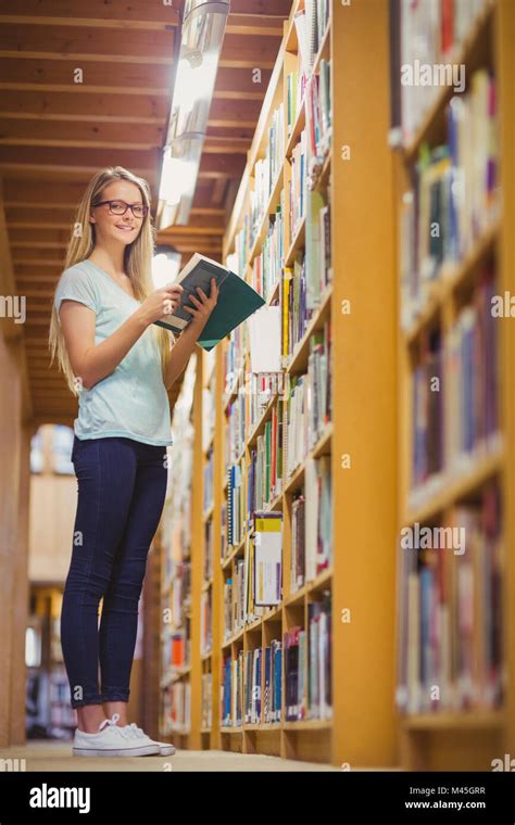 Blonde Student Reading Book Next To Bookshelf Stock Photo Alamy