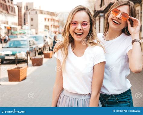 Twee Jonge Glimlachende Hipster Blonde Vrouwen In Kleren Van De De Zomer De Witte T Shirt Stock