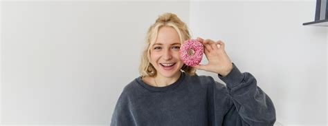Portrait en gros plan d une jolie jeune femme blonde montrant un donut rose près de son visage