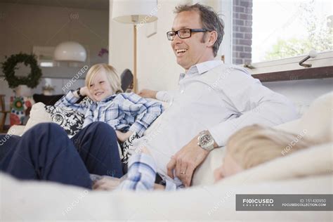 Mature Man Sitting With Sons On Sofa At Home Vertical Father Stock Photo