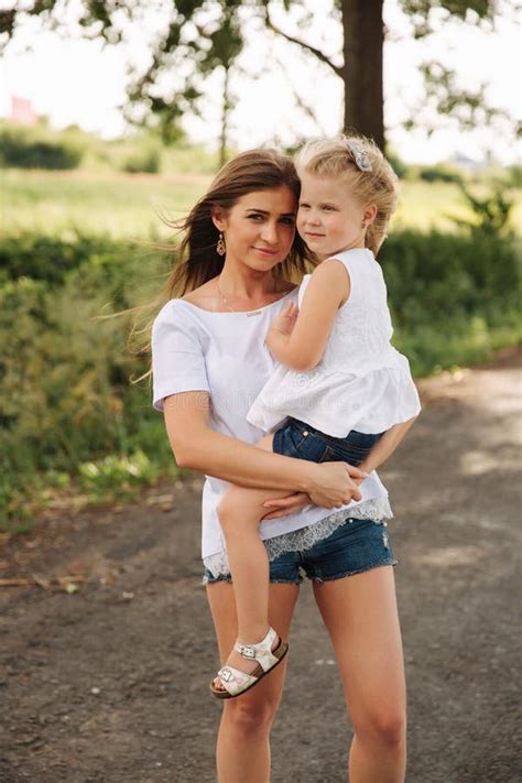 Attractive Mom And Blonde Hair Daughter Sits On Road Near Big Alley They Smile And Look To