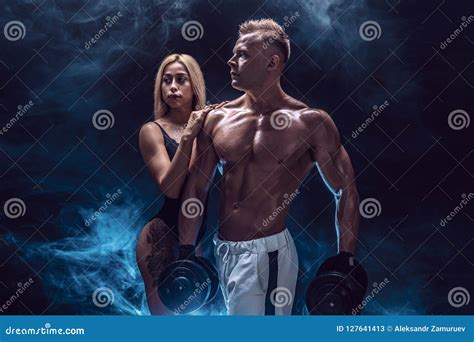 Attractive Couple A Slim Blonde Female And Handsome Shirtless Guy Posing At Studio On A Dark
