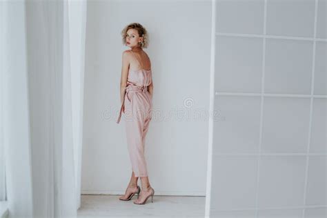 Beautiful Fashionable Blonde Woman In Pink Clothes Poses In White Room