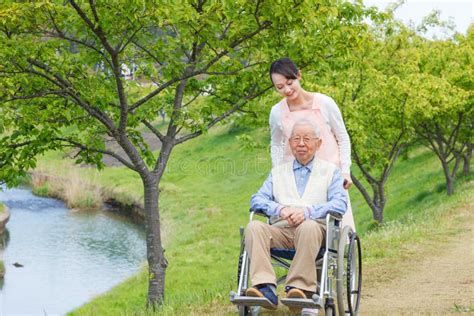 Asian Senior Man Sitting On A Wheelchair With Caregiver Pointing Stock