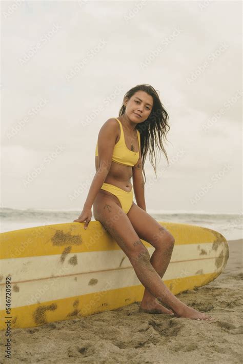 Foto De Asian Girl In Bikini At The Beach Is Sitting On A Surfboard Do Stock Adobe Stock