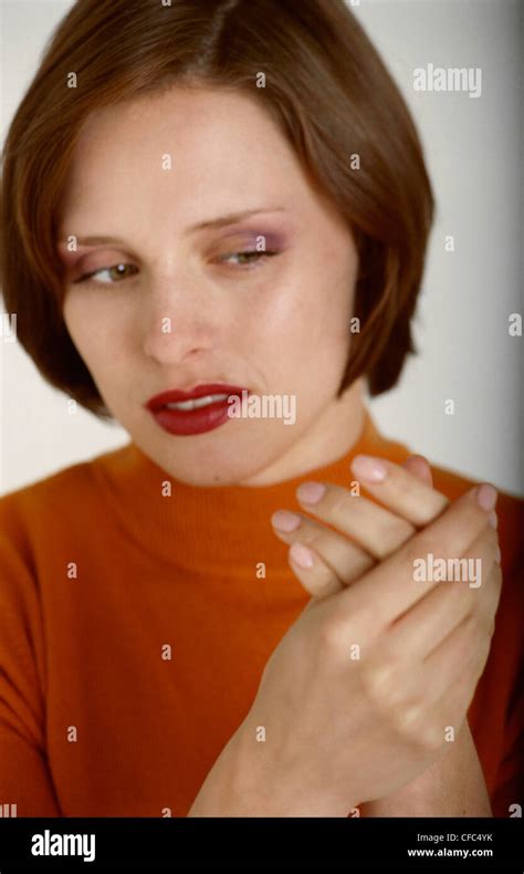 Female With Short Brunette Hair Wearing An Orange Top Massaging Her Hands Unsmiling Looking