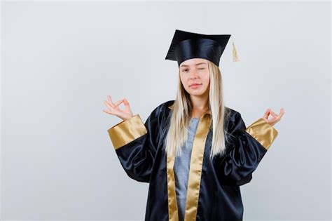 Fille blonde debout dans une pose de méditation un clin d œil dans une robe de graduation et