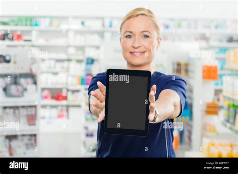 Portrait Of Mature Female Pharmacist Showing Digital Tablet With Blank Screen In Pharmacy Stock