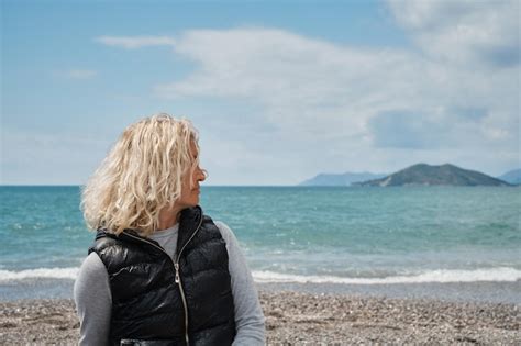 Erwachsene blonde europäische Frau allein an einem Kiesstrand mit blauem Meer und Himmel im