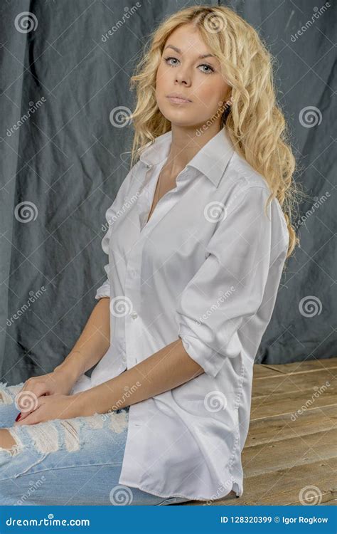 Blonde Hermoso Joven De La Muchacha En Una Camisa Blanca Y Vaqueros Con Huecos Imagen De Archivo