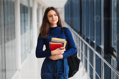 Cheerful Brunette Student Girl With Black Backpack Holds Books In Modern Building Female