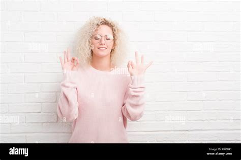 Junge blonde Frau mit lockigem Haar über weiße Mauer entspannen und Lächeln mit den Augen dabei