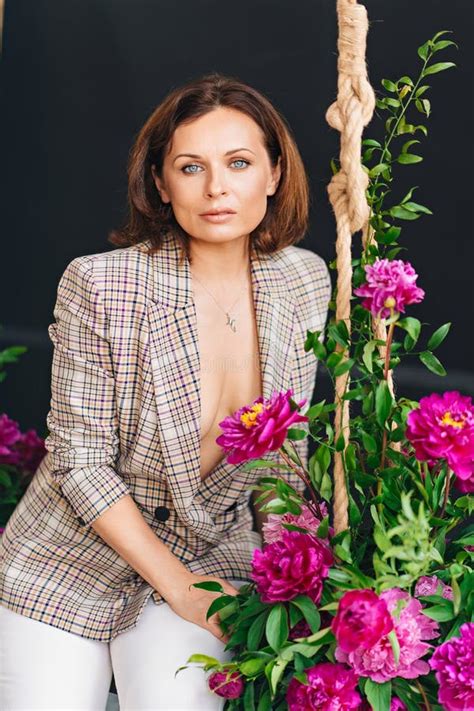 An Attractive Brunette Woman In A Plaid Jacket On A Swing With Peony Flowers Stock Photo