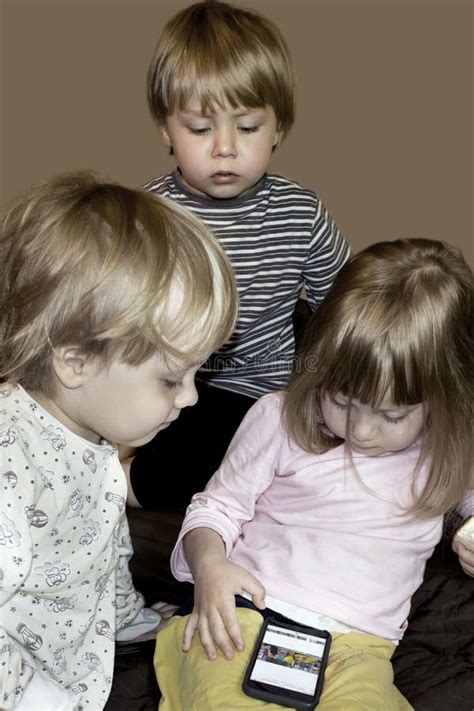 Kleine Nette Neugierige Blonde Dreiergruppen Passen Karikaturen Auf Smartphone Auf Stockbild