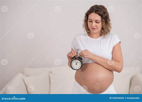 A Pregnant Woman With A Naked Belly Holds An Alarm Clock Intended Date Of Birth Stock Photo